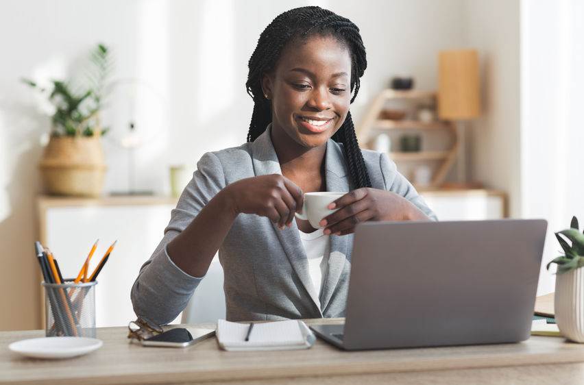 Mulher de negócios negra tomando café enquanto trabalha em um laptop em um escritório moderno